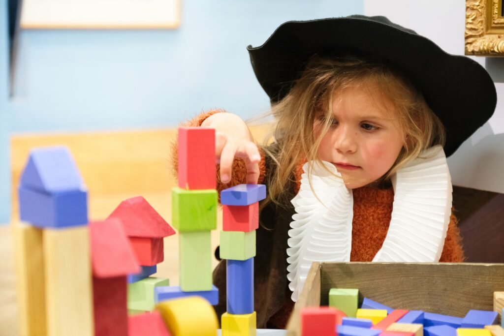 young girl wearing a white tudor ruff and black round hat playing with colourful wooden blocks in a museum gallery
